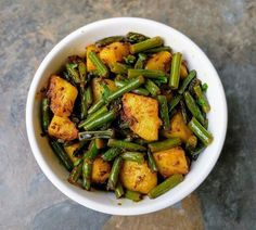 a white bowl filled with cooked green beans and tofu on top of a table