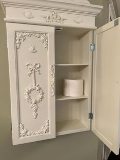 an open white cabinet with toilet paper on the shelf in front of it and a roll of toilet paper next to it