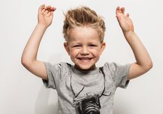 a little boy that is standing up with his hands in the air and smiling at the camera