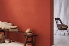 a wooden bench sitting in front of a red wall next to a chair and table