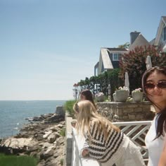 two women standing next to each other in front of a house near the ocean and water