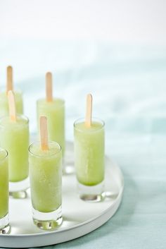 several glasses filled with green liquid and toothpicks sitting on a white platter