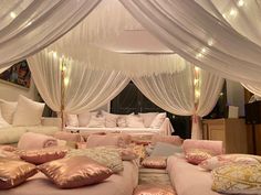 a bed room with lots of pillows on the floor and white drapes over it