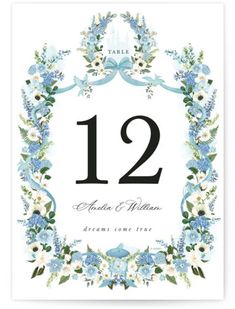 a wedding table number card with blue flowers and greenery on the front, in a floral frame