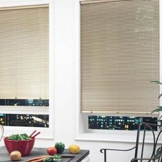 a kitchen with two windows covered in blinds and vegetables on the counter top next to it