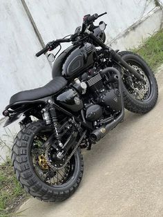 a black motorcycle parked on the side of a road next to a cement wall and grass