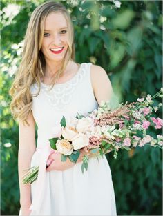 a woman holding a bouquet of flowers in her hands and smiling at the camera with greenery behind her