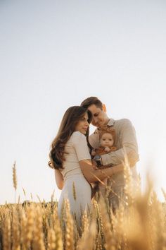 a man and woman holding a baby in a wheat field