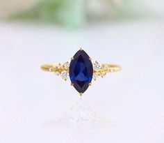 a gold ring with a blue stone and two diamonds on the side, sitting on top of a white surface