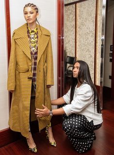 a woman kneeling down next to a mannequin wearing a yellow and black coat