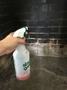 a hand holding a spray bottle in front of a brick oven