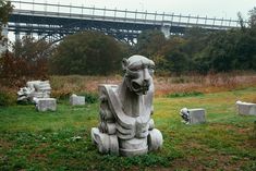 a stone lion statue sitting on top of a lush green field next to a bridge