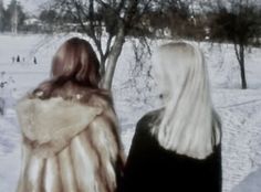 two women are standing in the snow looking at each other and one is wearing a fur coat