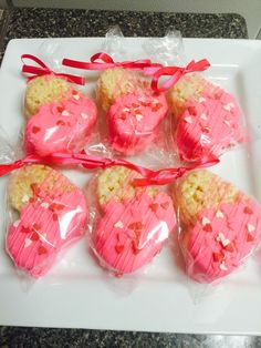 six heart shaped cookies wrapped in plastic on a white plate with red ribbon around them