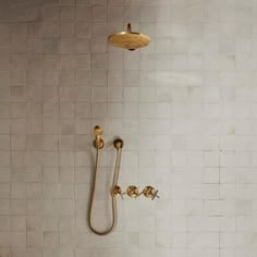 a shower head and hand shower in a white tiled bathroom with gold fixtures on the wall