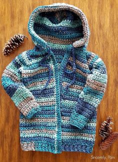 a crocheted jacket and pine cones on a wooden surface with the hood up