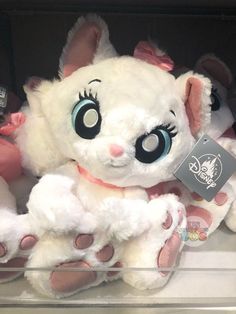 a white stuffed animal with blue eyes and pink ears sitting on display in a store