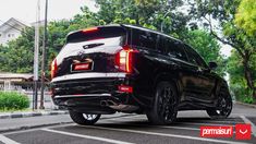 the rear end of a black suv parked in a parking lot next to some trees