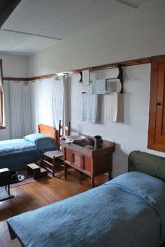 two beds in a room with wooden floors and white walls, one has blue sheets on it