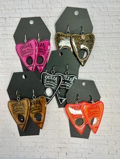 The unique pair of Ouija planchette earrings are crafted by hand, making each set a one-of-a-kind. The inking of each earring is done in a contrasting color to add a vibrant pop of style. Despite their large size, each earring is incredibly lightweight, and is designed to hang from a lever back for a secure and comfortable fit - even for those with stretched ears!Measurements~ 3 inches long~2 inches wide at widest point Planchette Earrings, Ouija Planchette, Hand Making, Stretched Ears, Gold Flakes, Mozambique, Contrasting Colors, Large Size, Color