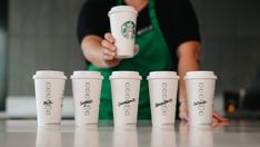 six starbucks cups lined up in front of a person