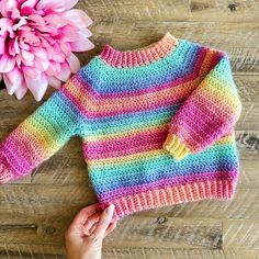 a hand holding a pink flower next to a colorful sweater