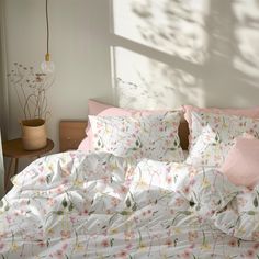 an unmade bed with pink and white flowers on it, next to a window