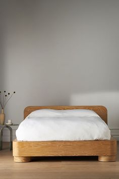 a bed sitting on top of a hard wood floor next to a white wall and vase with flowers