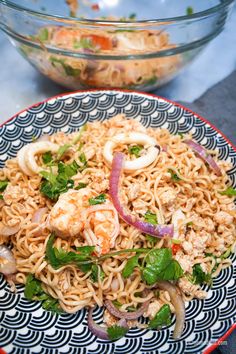 a plate full of noodles with shrimp and vegetables on it next to a bowl of salad