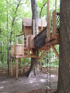 a tree house built into the side of a tree in a wooded area with swings and ladders