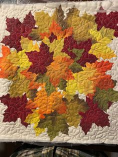 a quilted wall hanging with autumn leaves on it and someone's feet in the background