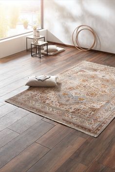 a rug on the floor in a room with wooden floors and white walls, next to a window