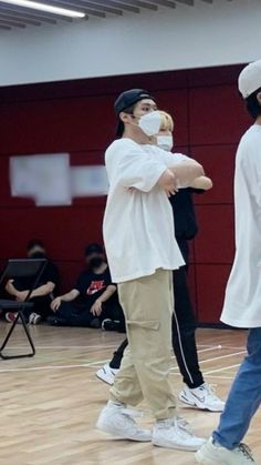 two men in white shirts and jeans standing on a basketball court with their arms crossed