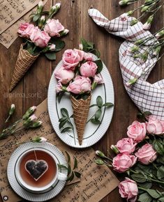 pink roses in ice cream cones next to a cup of tea and paper napkins