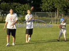 two men and a boy are playing football on the field with trees in the background