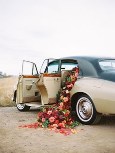 an old car with flowers on the back door is parked in front of a field