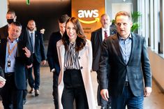 two women and three men are walking in an office building with the aws logo on the wall behind them