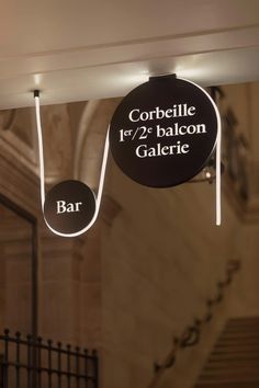 a bar sign hanging from the ceiling in front of some stairs and railings at night