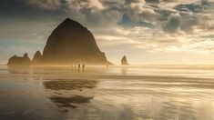 two people walking on the beach in front of an ocean stack at sunset or sunrise