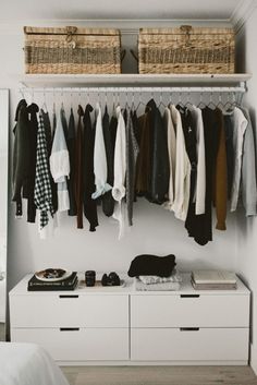 an organized closet with clothes hanging on the rails and baskets over the top of it