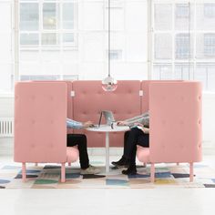 two people sitting at a table with laptops in front of them, both on pink chairs