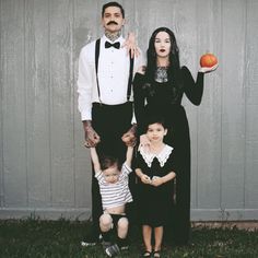 a family dressed up in halloween costumes standing next to each other and holding an orange pumpkin