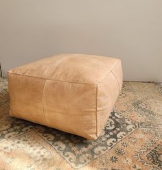 a large tan leather ottoman sitting on top of a carpeted floor next to a wall