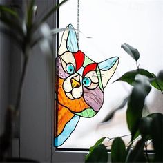 a stained glass cat sitting on top of a window sill next to a potted plant