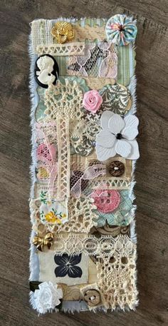 an altered piece of fabric with flowers and laces on the bottom, sitting on a wooden