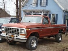 an old red pick up truck parked in front of a blue house