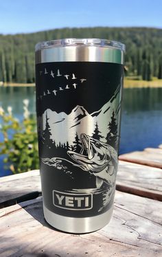 a yeti cup sitting on top of a wooden table next to a body of water