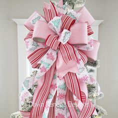 a large pink and white bow on top of a christmas tree