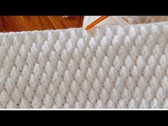 a white crocheted blanket with an orange pencil on top of it and a wooden floor in the background