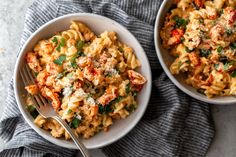 two bowls filled with pasta and vegetables on top of a blue towel next to a fork